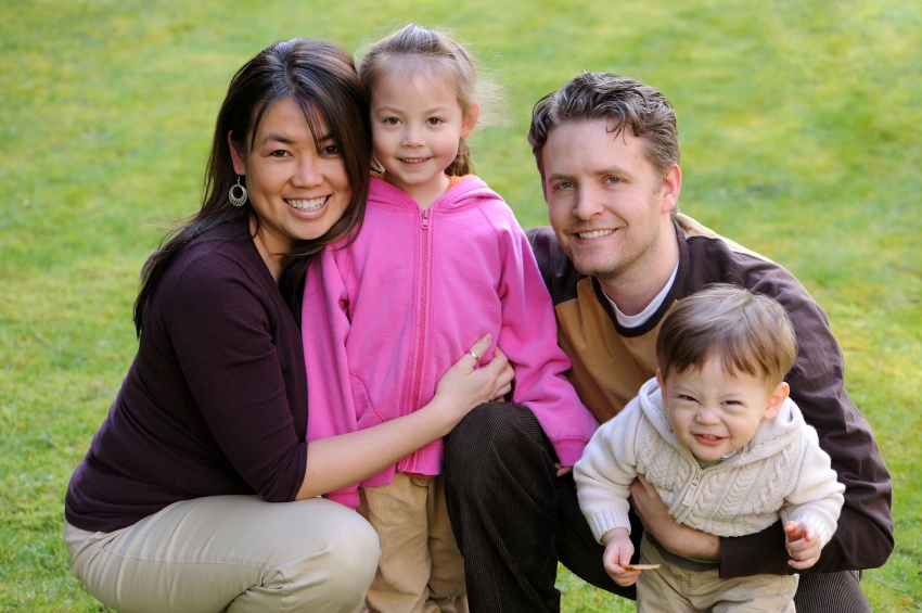 diverse family smiles / cuddling together outdoors / with grass in behind